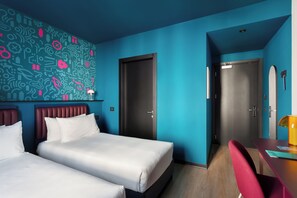 A hotel room with two beds, a desk, and a chair. There are two doors and a wall with a blue and white pattern. - CX Milan NoM (Novate Milanese)