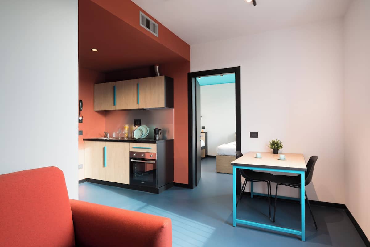 A modern room with a kitchen area, a dining table with chairs, and a red sofa.