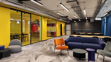 A modern office space with a yellow and blue color scheme, featuring a large sofa, multiple tables, and chairs.