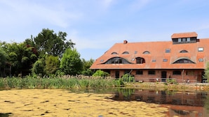 A large brick building with a red-tiled roof, surrounded by a pond with lily pads and reeds. - Rustic-style Apartment in Buschenhagen With Garden (Niepars)