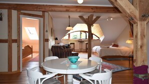 A cozy, well-lit room with a round dining table, white chairs, a bed, and a kitchen area. - Rustic-style Apartment in Buschenhagen With Garden (Niepars)