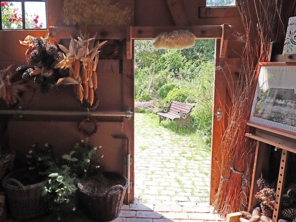 A rustic interior with a wooden door leading to a garden, shelves with dried corn and pinecones, and a wicker basket. - Rustic-style Apartment in Buschenhagen With Garden (Niepars)