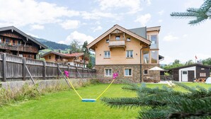 A wooden house with a stone facade, a balcony, and a fenced backyard. - Central Apartment With Balcony, Terrace, Garden, Deckchairs (Brixen im Thale)