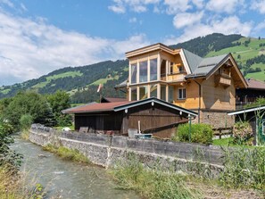 A wooden house with a stone wall and a river in the foreground. - Central Apartment With Balcony, Terrace, Garden, Deckchairs (Brixen im Thale)