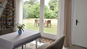 A dining area with a table set for two, a blue vase with flowers, and a view of a garden through glass doors. - Modern Bungalow in Blowatz Near Sea (Blowatz)