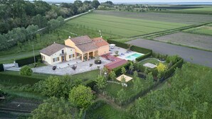 A large house with a swimming pool, surrounded by well-maintained gardens and fields.