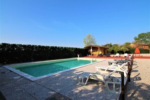 Une piscine avec des chaises longues, un petit bâtiment et une haie.