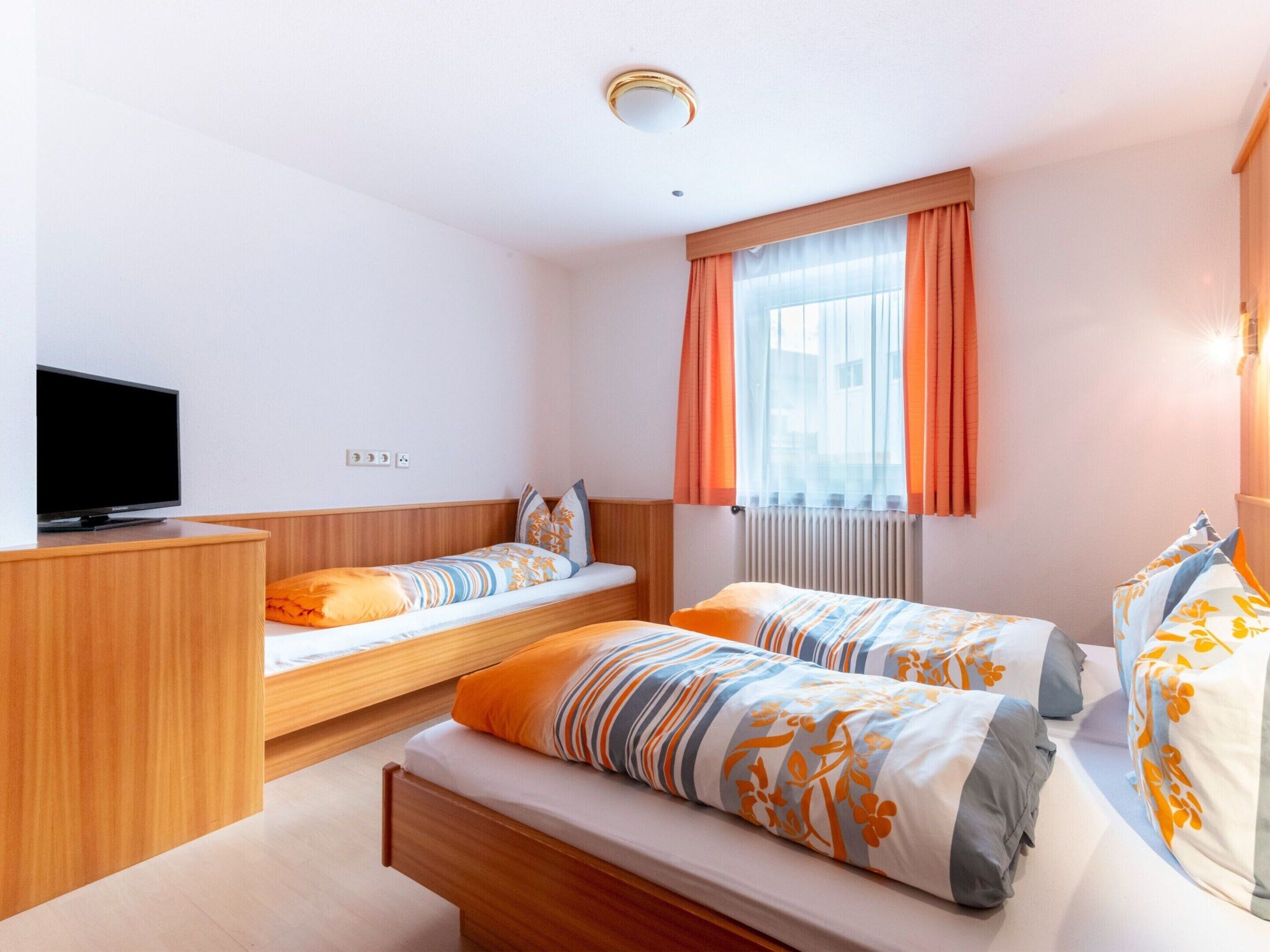 Une chambre d’hôtel avec deux lits simples, un bureau en bois, une télévision et une fenêtre avec des rideaux.