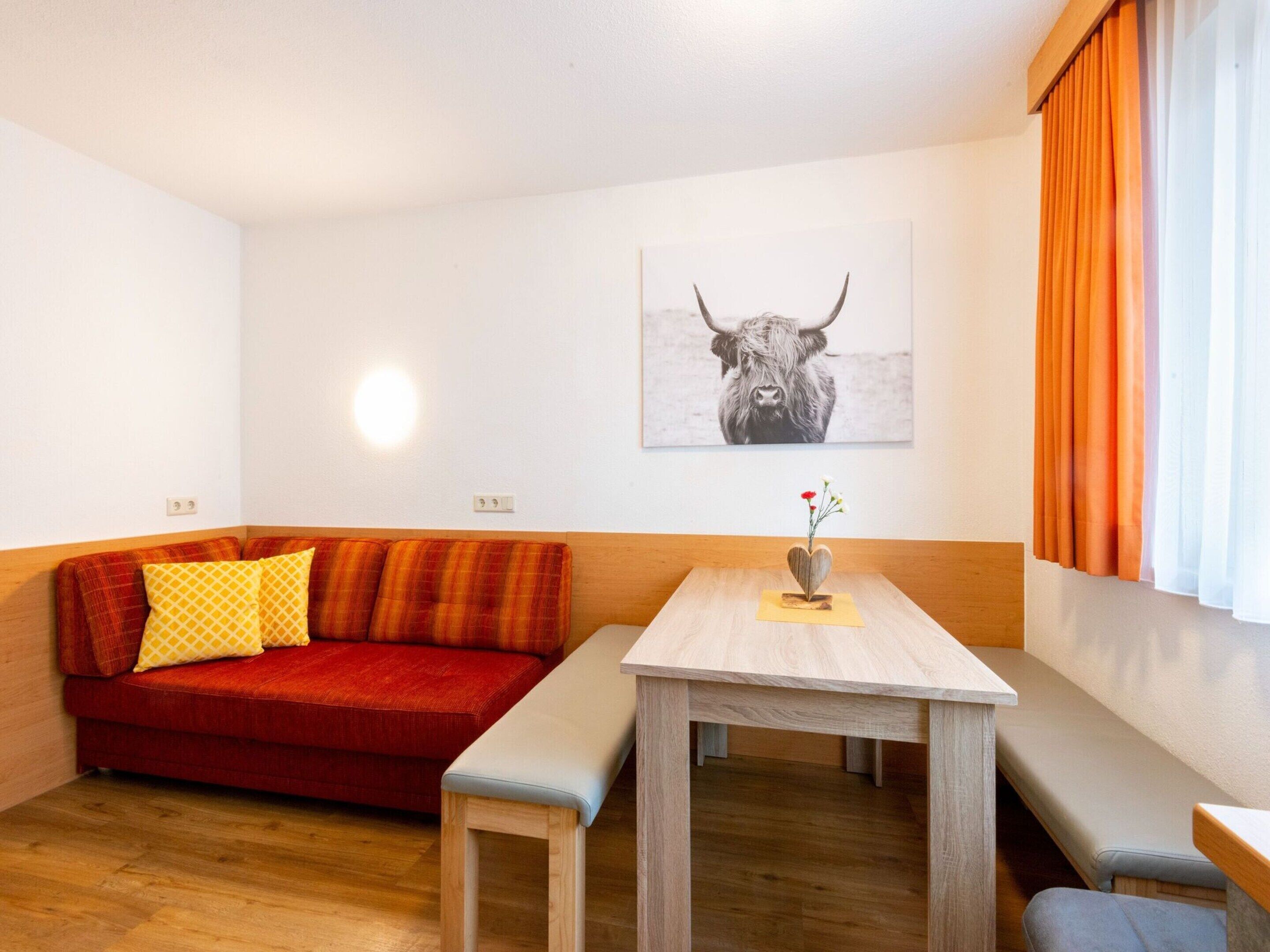 Une pièce chaleureuse avec un canapé rouge, une table en bois ornée d’un vase et un tableau représentant un taureau accroché au mur.
