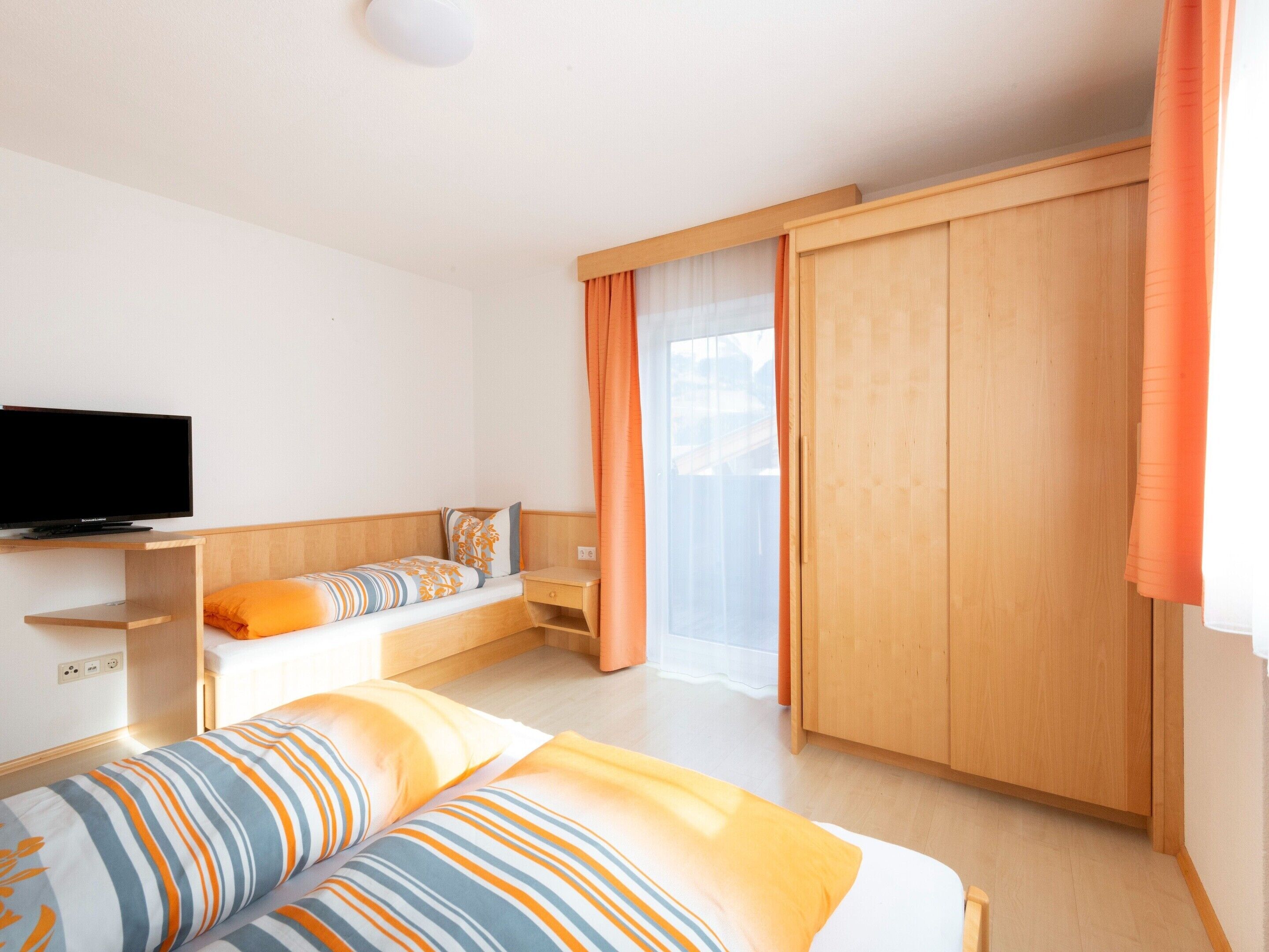A hotel room with a bed, a TV, a wooden wardrobe, and a window with curtains.