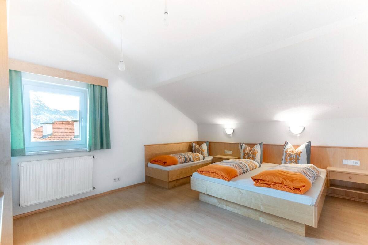 A bedroom with a large bed, two bedside tables, a window with curtains, and a radiator.