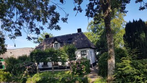 A house with a thatched roof, surrounded by lush greenery and a waterway. - Attractive Farmhouse in Giethoorn With Garden (Giethoorn)