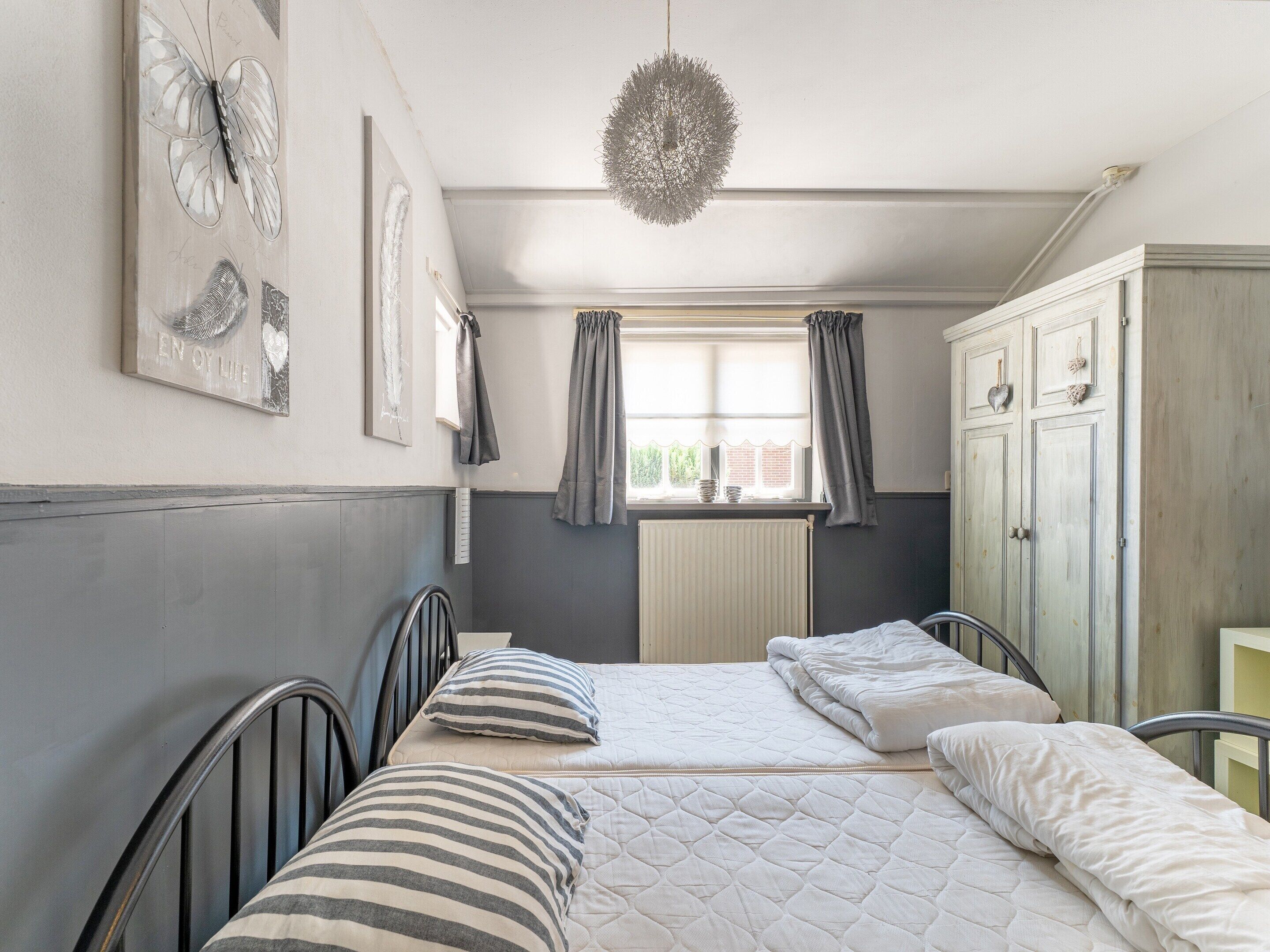 A bedroom with two beds, a radiator, a window with curtains, and a wardrobe.