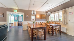 A spacious dining area with a long wooden table and chairs, a bench in the foreground, and a window with curtains. - Attractive Farmhouse in Giethoorn With Garden (Giethoorn)