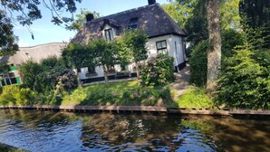 A house with a thatched roof, surrounded by lush greenery and a calm waterway. - Attractive Farmhouse in Giethoorn With Garden (Giethoorn)