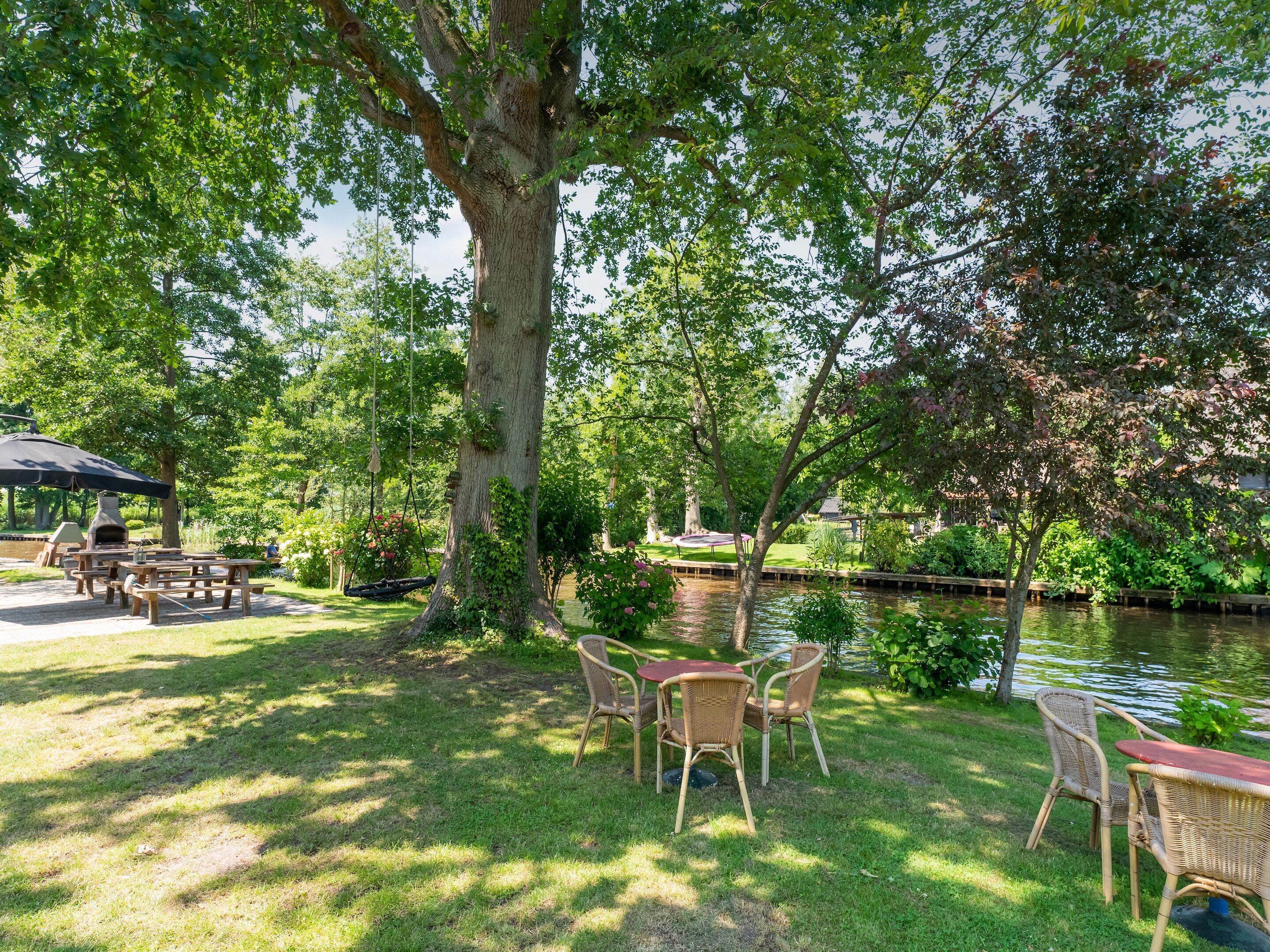 A serene outdoor patio area with picnic tables and chairs, surrounded by lush greenery and a body of water.