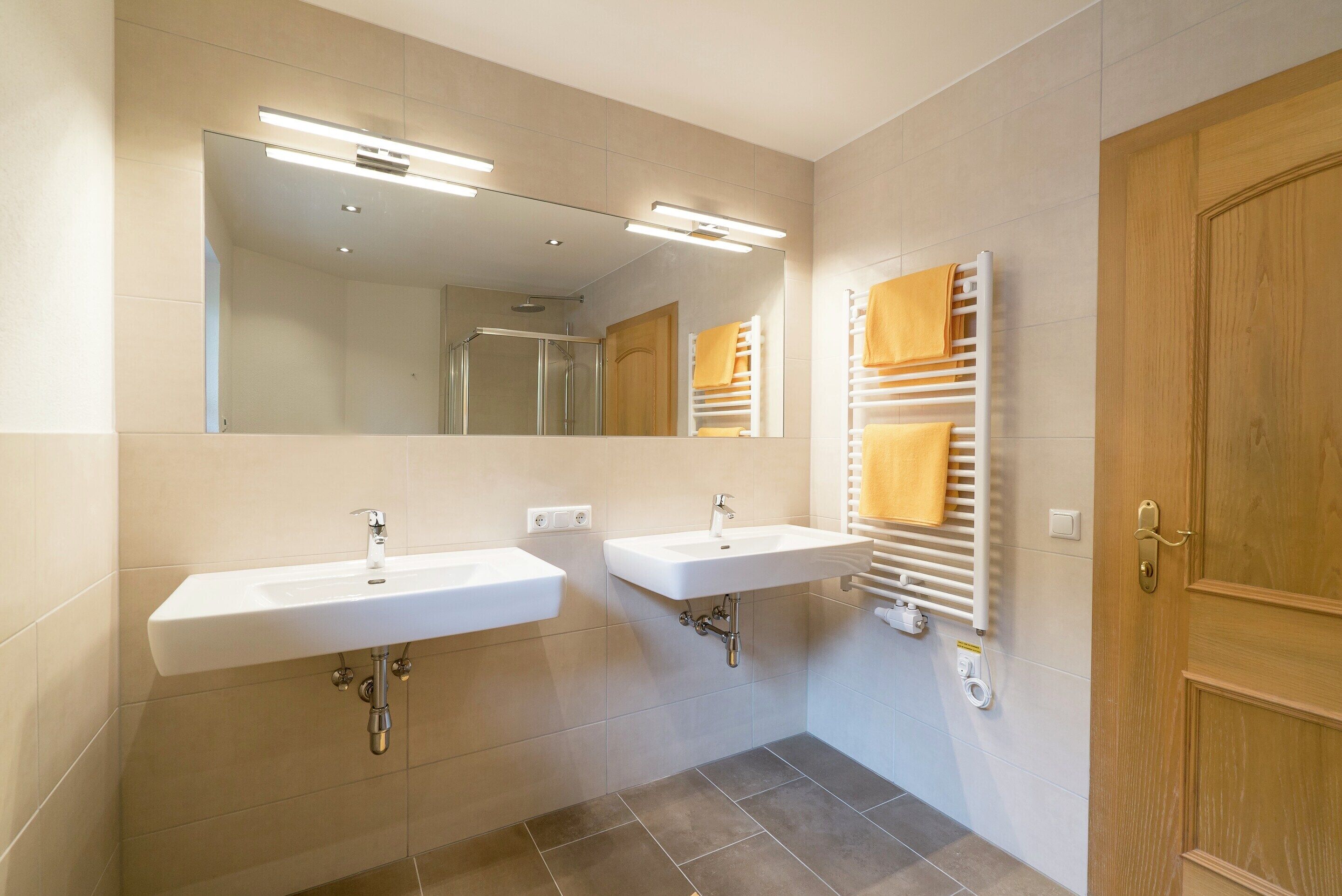 A modern bathroom with two sinks, a mirror, and a towel rack.
