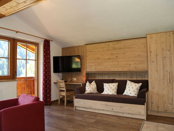A cozy room with a wooden sofa, a television mounted on the wall, and a desk with a chair. - Luxurious Holiday Home in Saalbach-hinterglemm With Barbecue (Viehhofen)