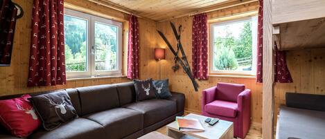 Interior acogedor de una cabaña con un sofá marrón, un sillón rosa y techo de madera.