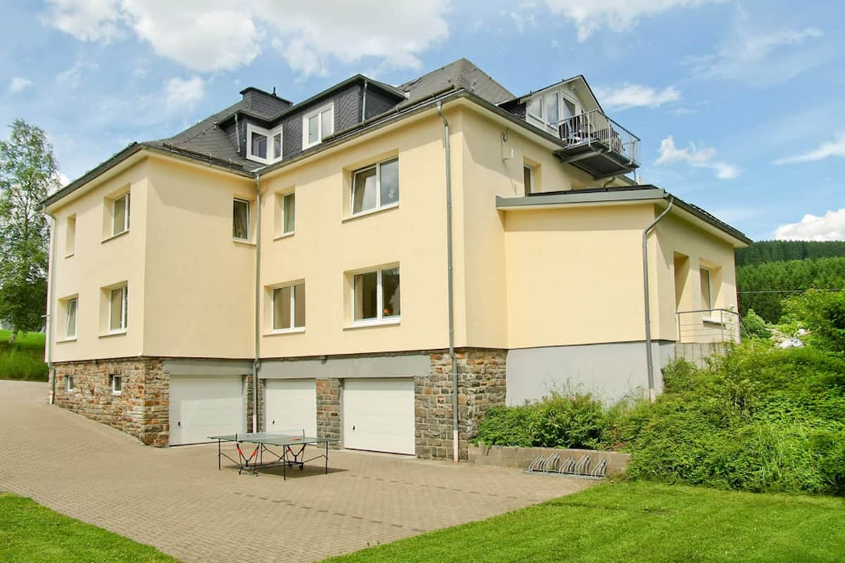 A two-story residential building with a paved driveway, a table tennis table, and a stone foundation.