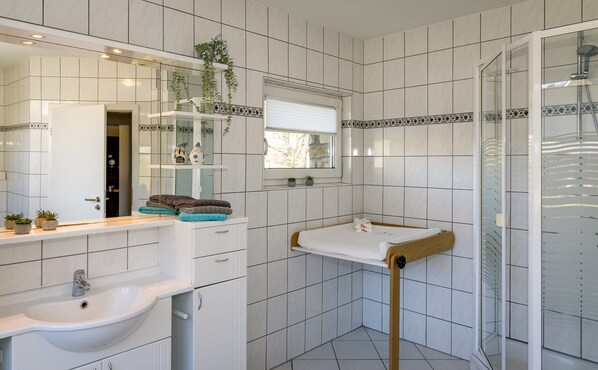 A modern bathroom with white tiles, a sink, a mirror, and a shower. - Large Apartment in the Beautiful Sauerland With Garden, Patio and Sauna (Erndtebrück)