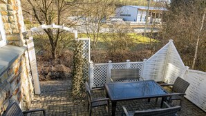 Egy szabadtéri terasz, ahol van egy asztal és néhány szék, egy fehér kerítés és egy kőből épített fal.