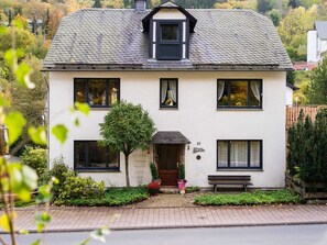 A two-story house with a white exterior, multiple windows, and a small front porch with a bench. - Large, Detached Holiday Home in Willingen With Garden (Willingen)