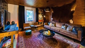 A cozy living room with a wooden ceiling, a leather sofa, a coffee table, a bookshelf, and a large fur rug. - Large, Detached Holiday Home in Willingen With Garden (Willingen)