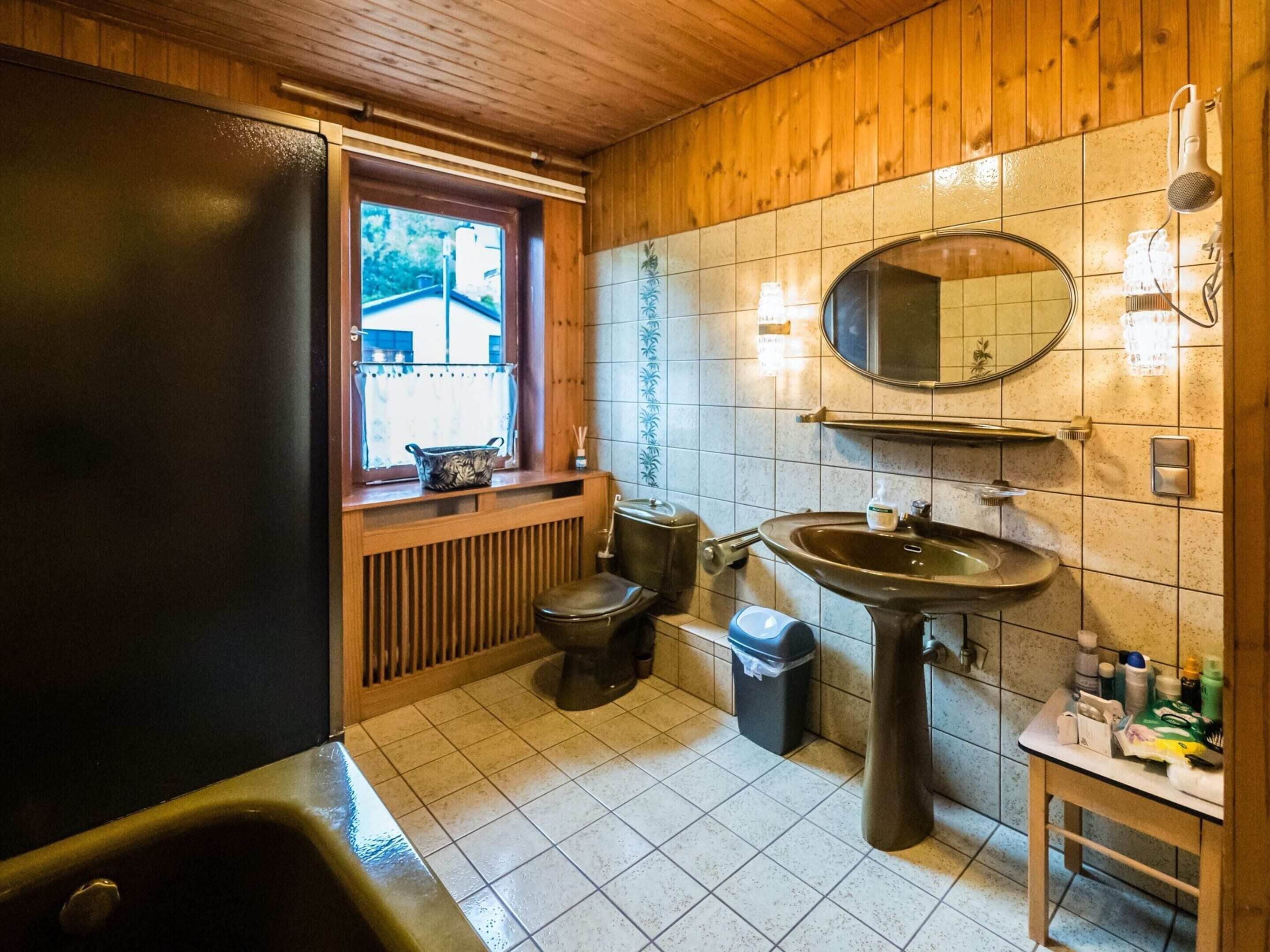 Ein kleines Badezimmer mit Fenster, Waschbecken, Toilette und Badewanne.