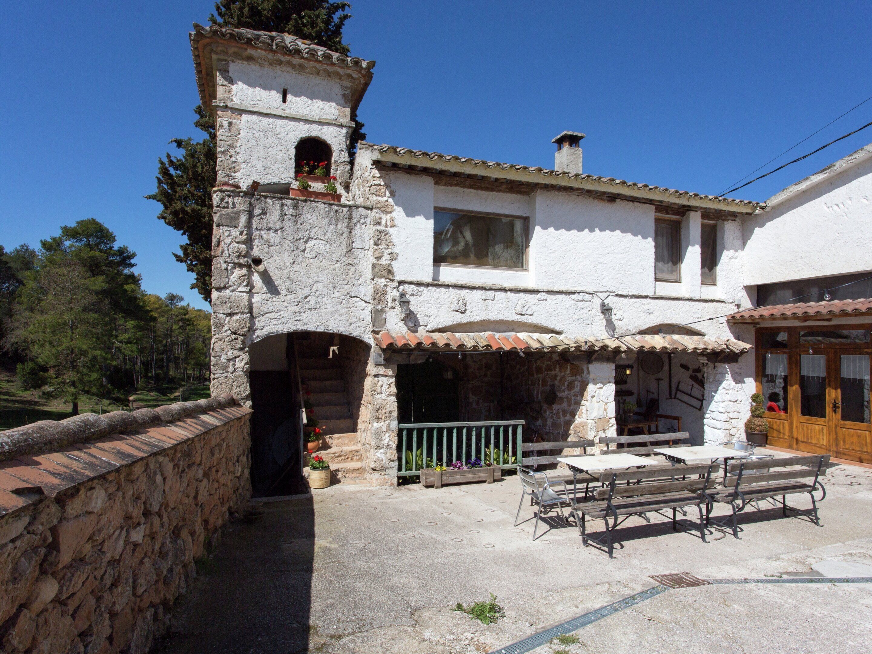 A stone building with a bell tower, a patio with benches, and a wooden door.