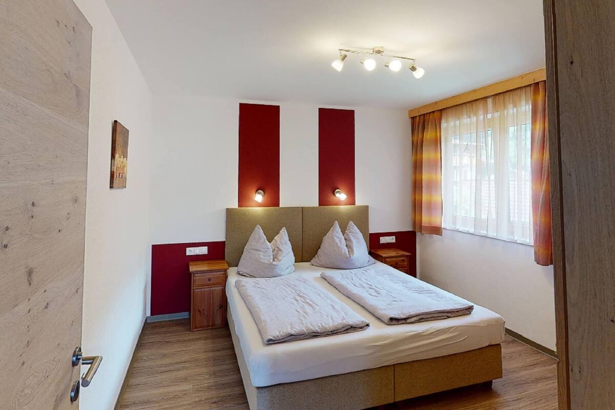 Habitación de hotel con una cama grande, dos mesitas de noche, una lámpara de pared y una ventana con cortinas.