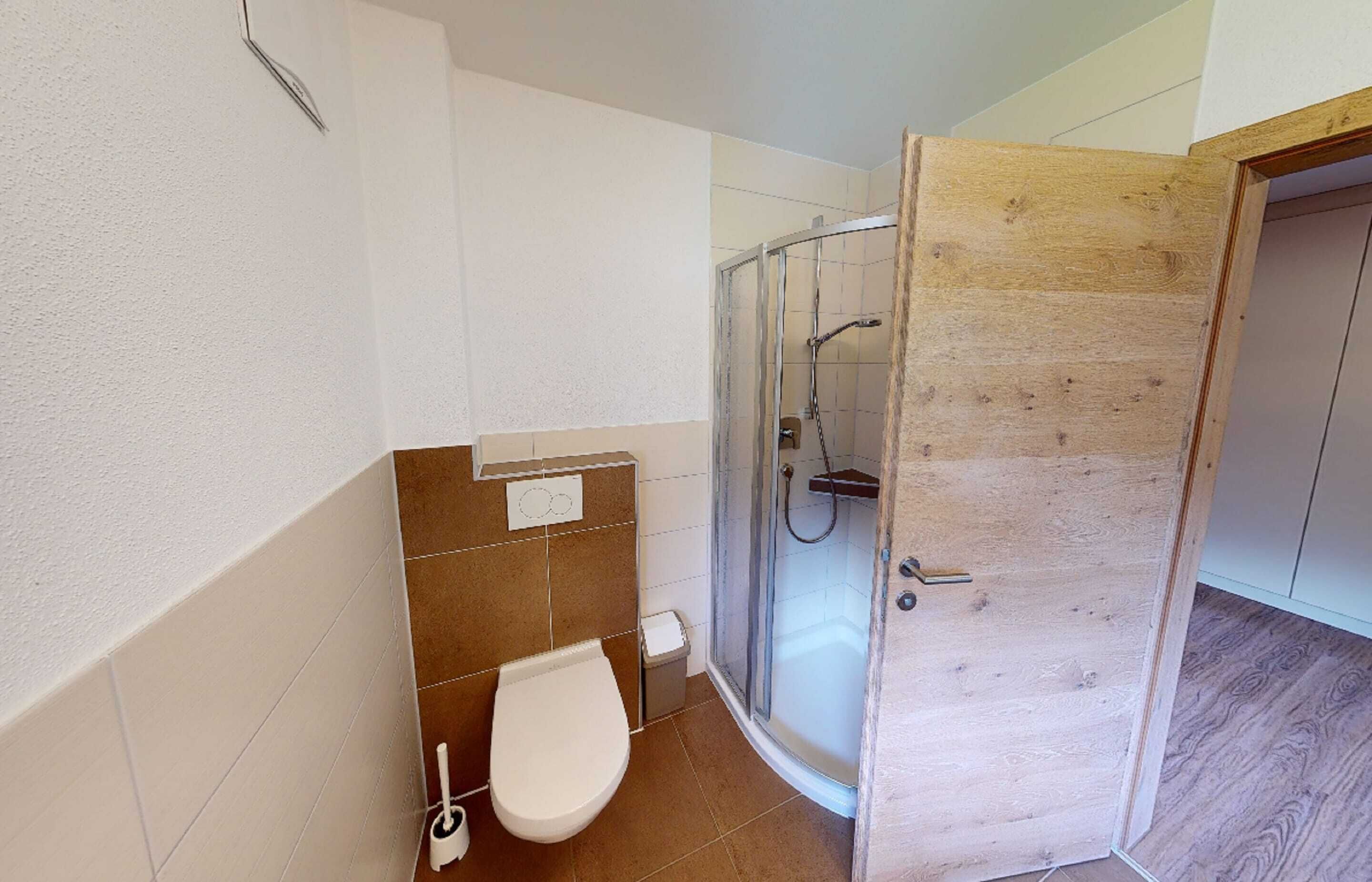 A bathroom with a toilet, a shower enclosure, and a wooden door.