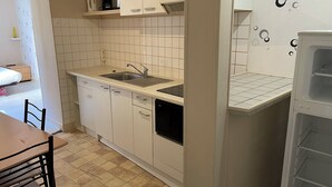 Cocina compacta con armarios blancos, un lavamanos y lavavajillas.