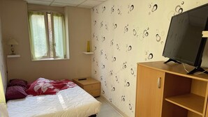 Un dormitorio con cama, televisión sobre un mueble de madera, mesita de noche y ventana con cortinas.