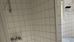 Zona de ducha en esquina con paredes de azulejos blancos y una bañera blanca.