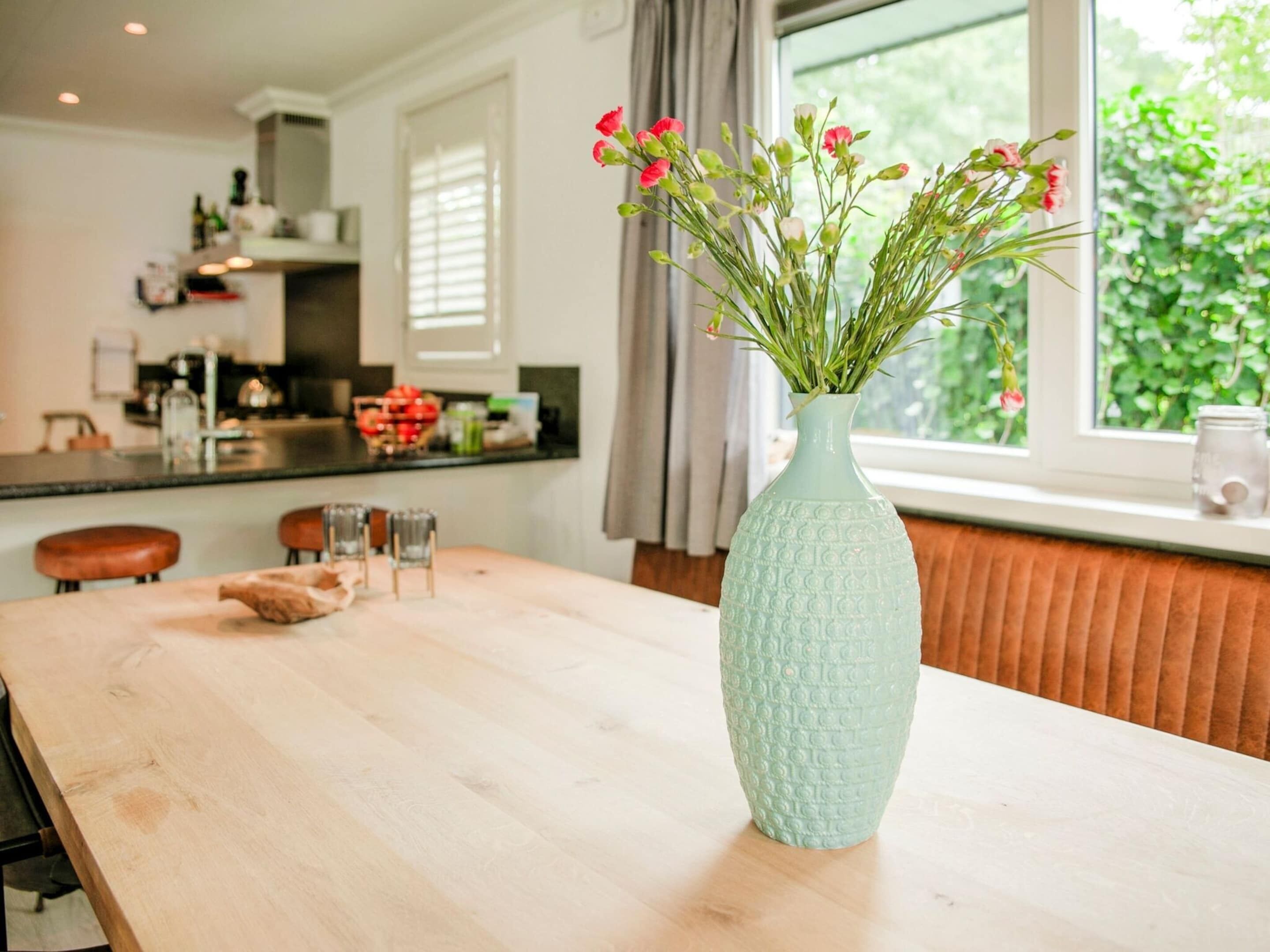 A kitchen with a wooden table, a vase with flowers, and a window with greenery outside.