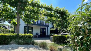 A modern house with a covered patio, surrounded by well-maintained hedges and a sandy area. - Lovely Holiday Home in Kaatsheuvel With Bubble Bath (Kaatsheuvel)