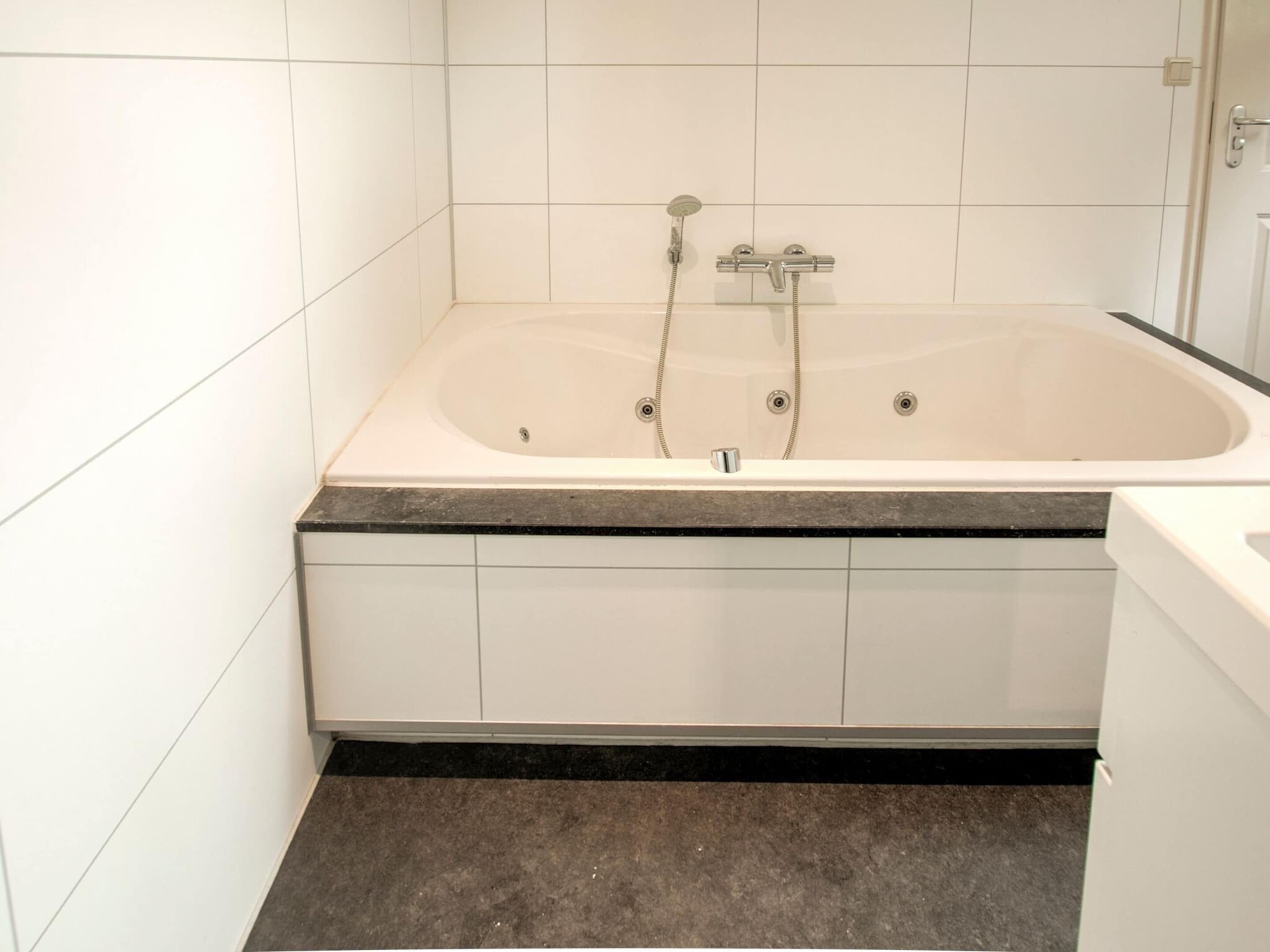 A modern bathroom with a freestanding bathtub, white tiled walls, and a dark floor.