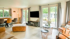 A modern living room with a TV, seating, and a view of the outdoors. - Lovely Holiday Home in Kaatsheuvel With Bubble Bath (Kaatsheuvel)