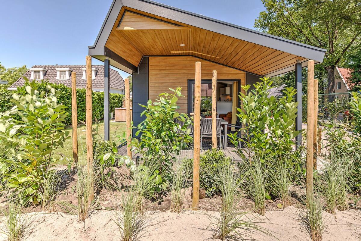 Une maison moderne dotée d’une terrasse en bois, entourée de différentes plantes et d’arbres.
