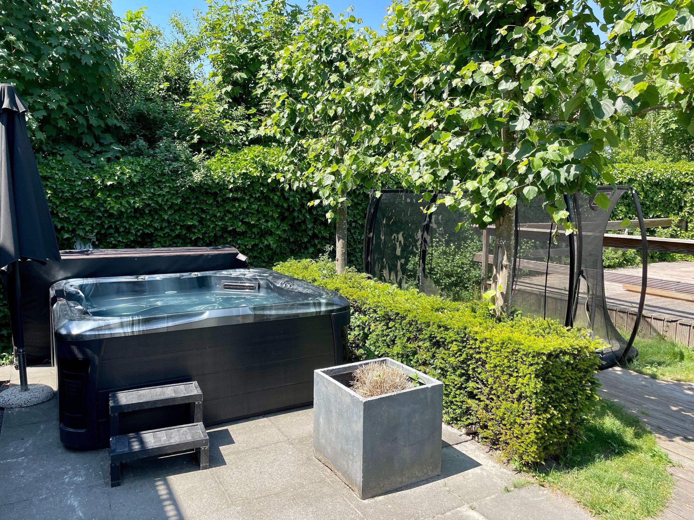 A hot tub with a bench and a planter, surrounded by greenery and a fence.