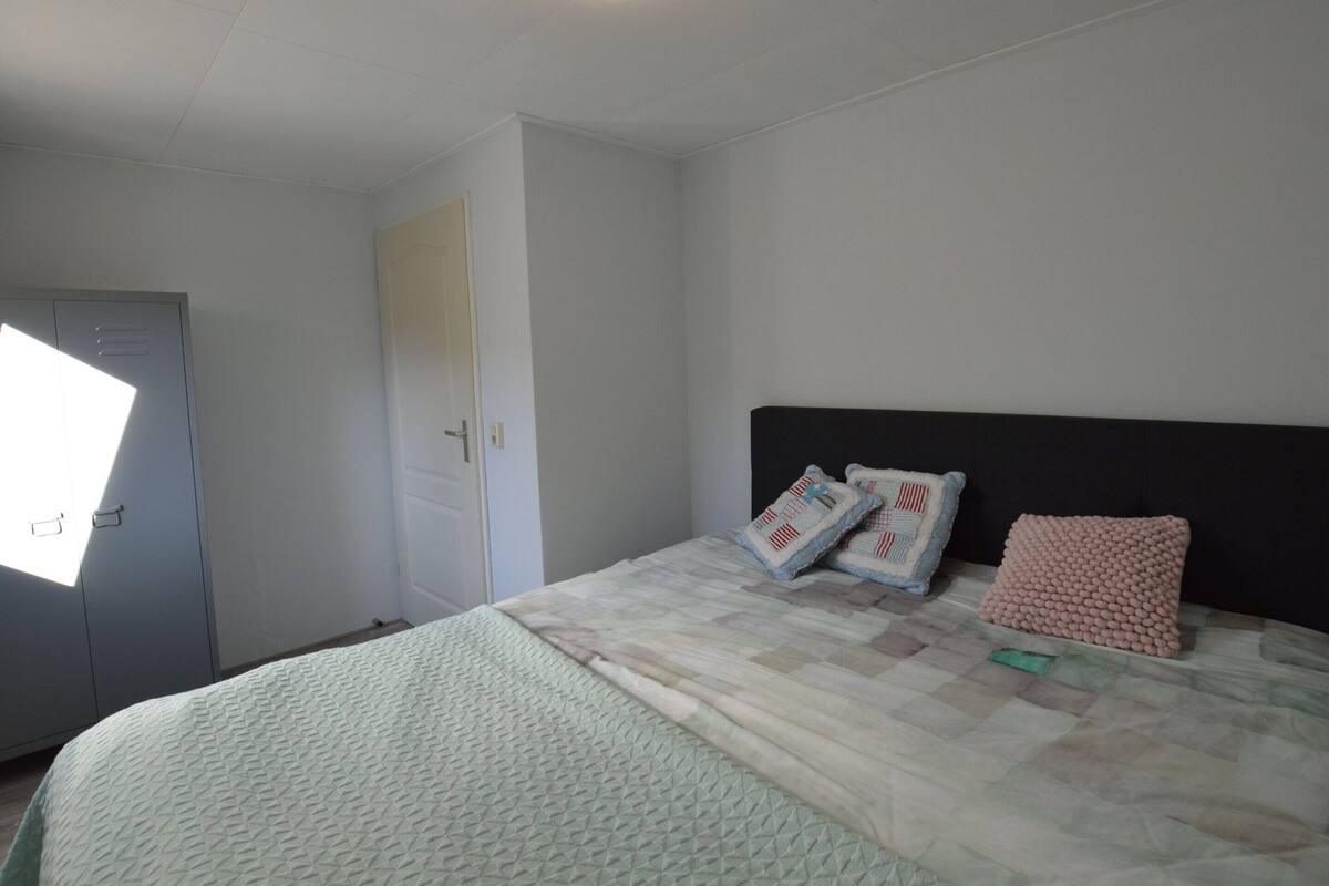 Une chambre à coucher avec un lit, des oreillers, une tête de lit, une armoire et une porte.