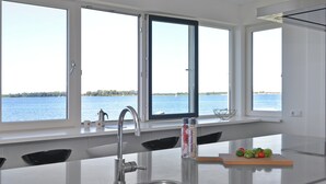 A modern kitchen with a large island, stainless steel sink, and a view of the water. - Waterfront Penthouse With Roof Terrace and Private Jetty (Kamperland)
