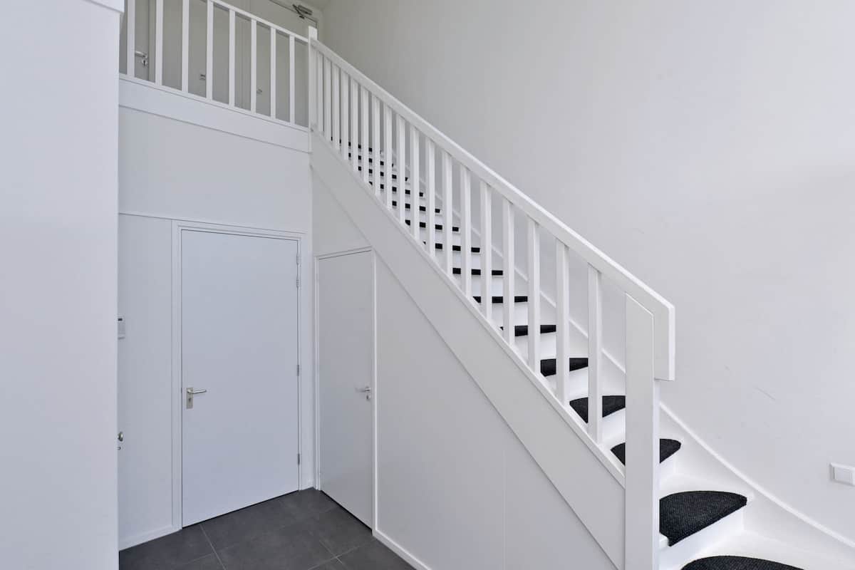 Un escalier avec des rampes blanches et des marches recouvertes de moquette noire, menant à un palier doté de deux portes blanches.