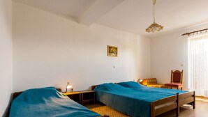 A room with two wooden beds, a small table with a lamp, a chair, and a window with curtains.