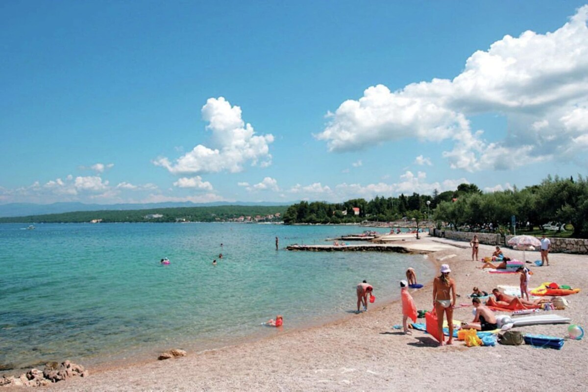 A beach with clear water, people swimming, and beachgoers relaxing.