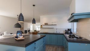 Una cocina moderna con armarios azules, una isla central, luces colgantes y una estufa integrada.