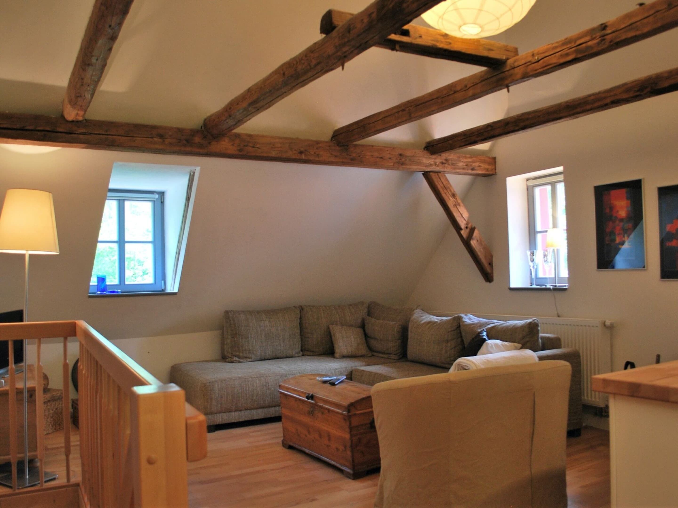 A cozy living room with exposed wooden beams, a sofa, a wooden chest, and a lamp.