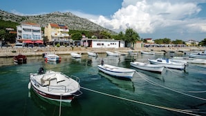 A marina with several boats docked, a stone wall, and buildings with balconies and shops. - Modern Apartment in Starigrad Paklenica With Barbecue (Starigrad)