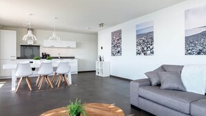 A modern living room with a gray sofa, a wooden coffee table with a plant, and a dining area with white chairs and a kitchen in the background. - Exclusive Apartment on the Ground Floor Directly Located on the Water (Kamperland)
